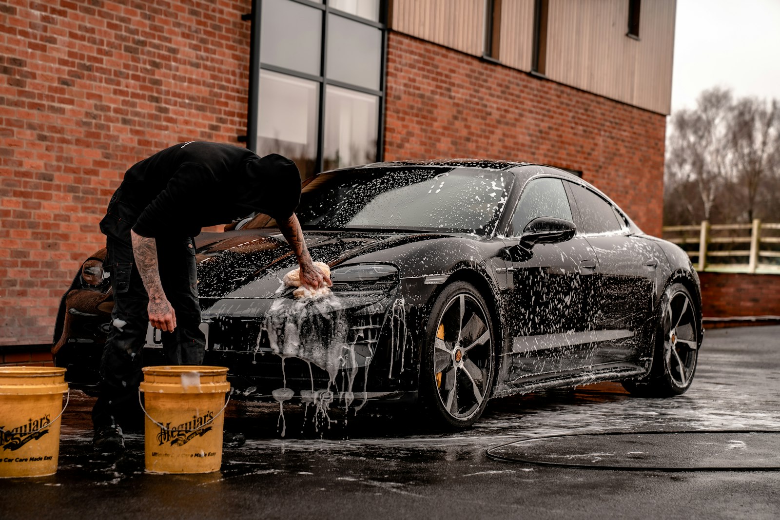 Detailer hand-washing a black car with foam